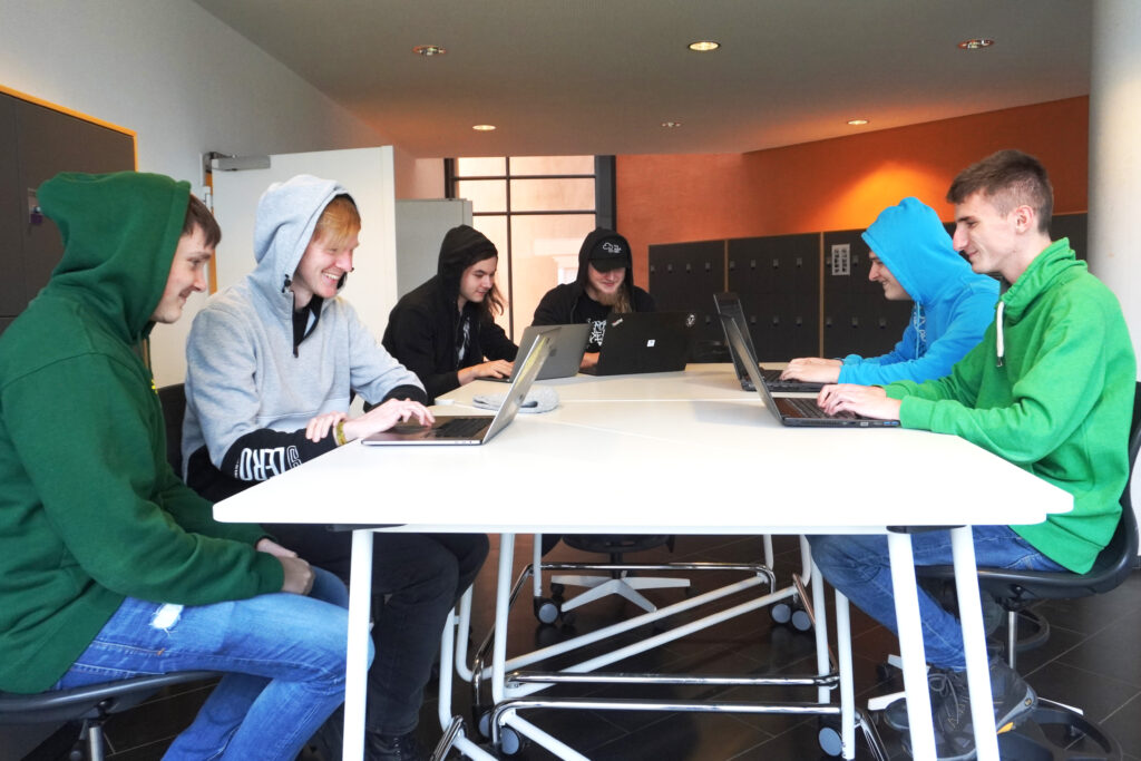 Teams beim Programmieren mit Laptops an einem Gruppentisch für den Wettbewerb Capture the Flag
